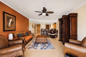 A spacious living room with leather sofas, a patterned rug, a ceiling fan, and a dining area with wooden furniture.