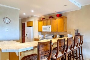 A kitchen with wooden cabinets, a microwave, a refrigerator, and a dining area with a long table and chairs.