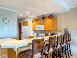 A kitchen with wooden cabinets, a white refrigerator, a microwave, and a stove. There is a dining table with chairs.