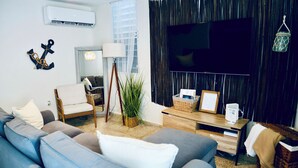 A modern living room with a blue sofa, a wooden coffee table, and a TV mounted on a dark wall.