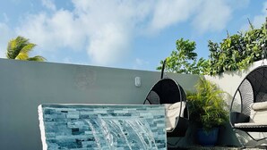 A swimming pool with a waterfall feature, surrounded by lounge chairs and potted plants.