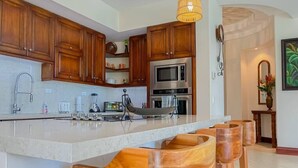A modern kitchen with wooden cabinets, a large island with stools, stainless steel appliances, and a hanging light fixture. - Bella Vista Ocean View Retreat at Los Sueños (Herradura)