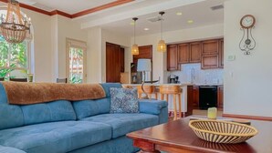 A living room with a blue sofa, wooden dining table, and kitchen in the background. - Bella Vista Ocean View Retreat at Los Sueños (Herradura)