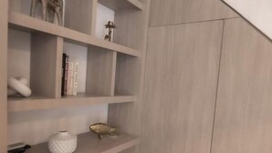 A room with a wooden shelving unit containing various decorative items, a potted plant, and a large wardrobe. - Private 3 Bedroom Home with Patio in Walled City (Cartagena)