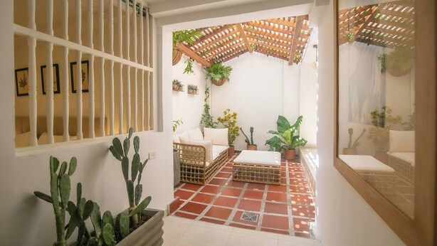 A sunlit room with a tiled floor, a wooden bench, a white sofa, and a ceiling fan. - Private 3 Bedroom Home with Patio in Walled City (Cartagena)