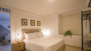 A bedroom with a bed, bedside tables, a window with a plant, and framed pictures on the wall. - Private 3 Bedroom Home with Patio in Walled City (Cartagena)