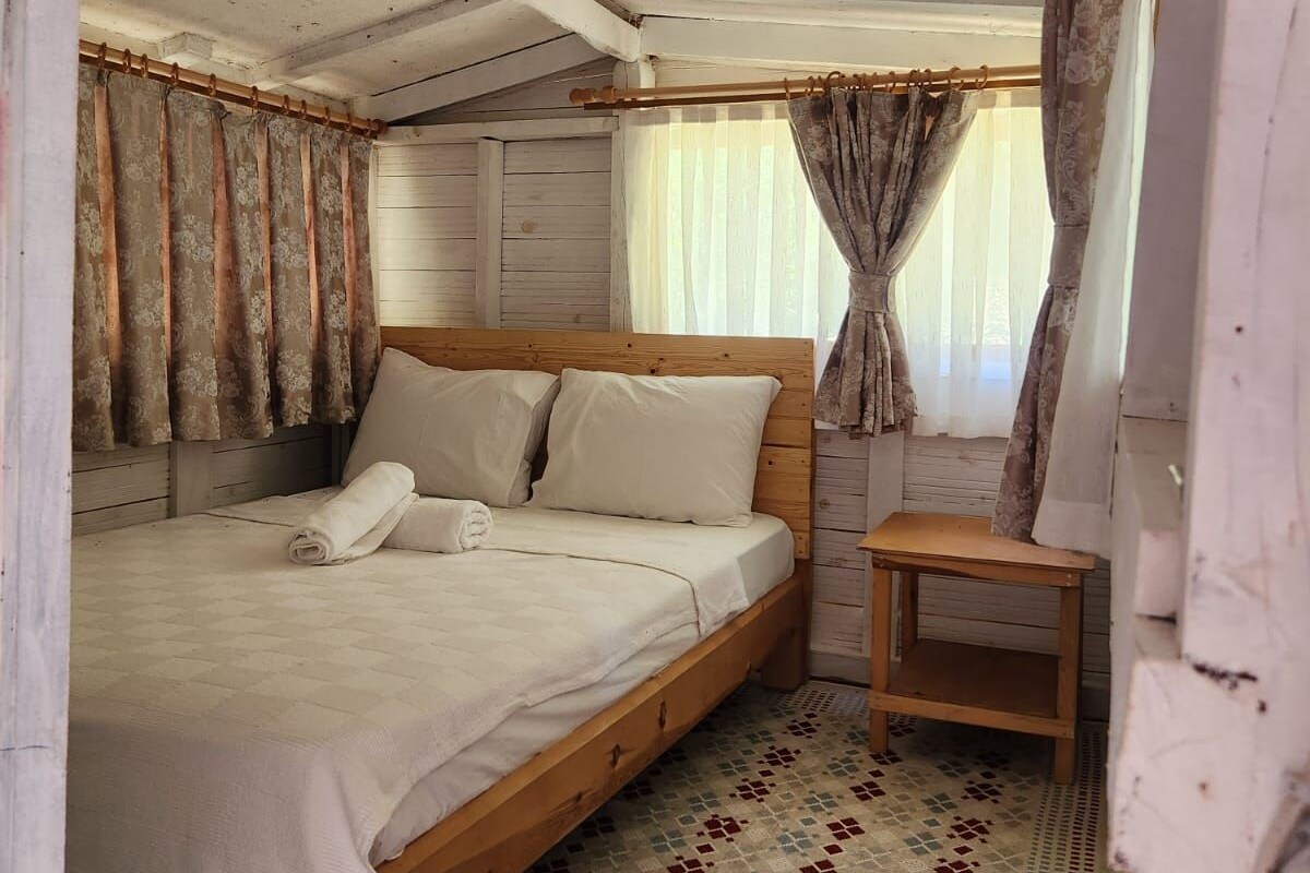 Um quarto rústico de madeira com uma cama, uma mesa pequena e uma janela com cortinas.