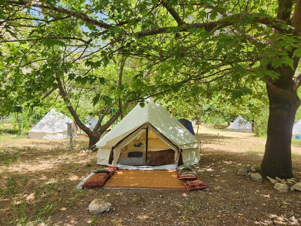 A treehouse-style tent with a pitched roof, surrounded by trees, on a grassy area with a woven mat and cushions on the ground. - Kelebekler Vadisi Butterfly Valley (Fethiye)