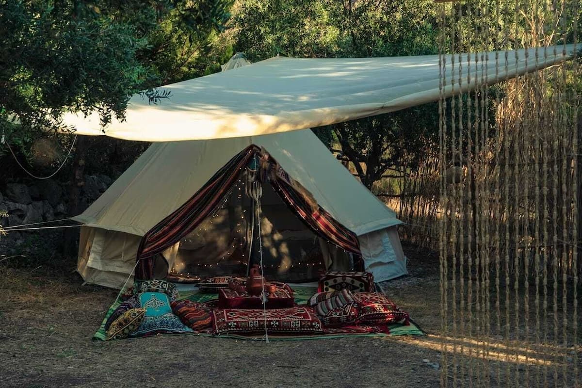 Una carpa con toldo, rodeada de árboles y una manta con cojines.