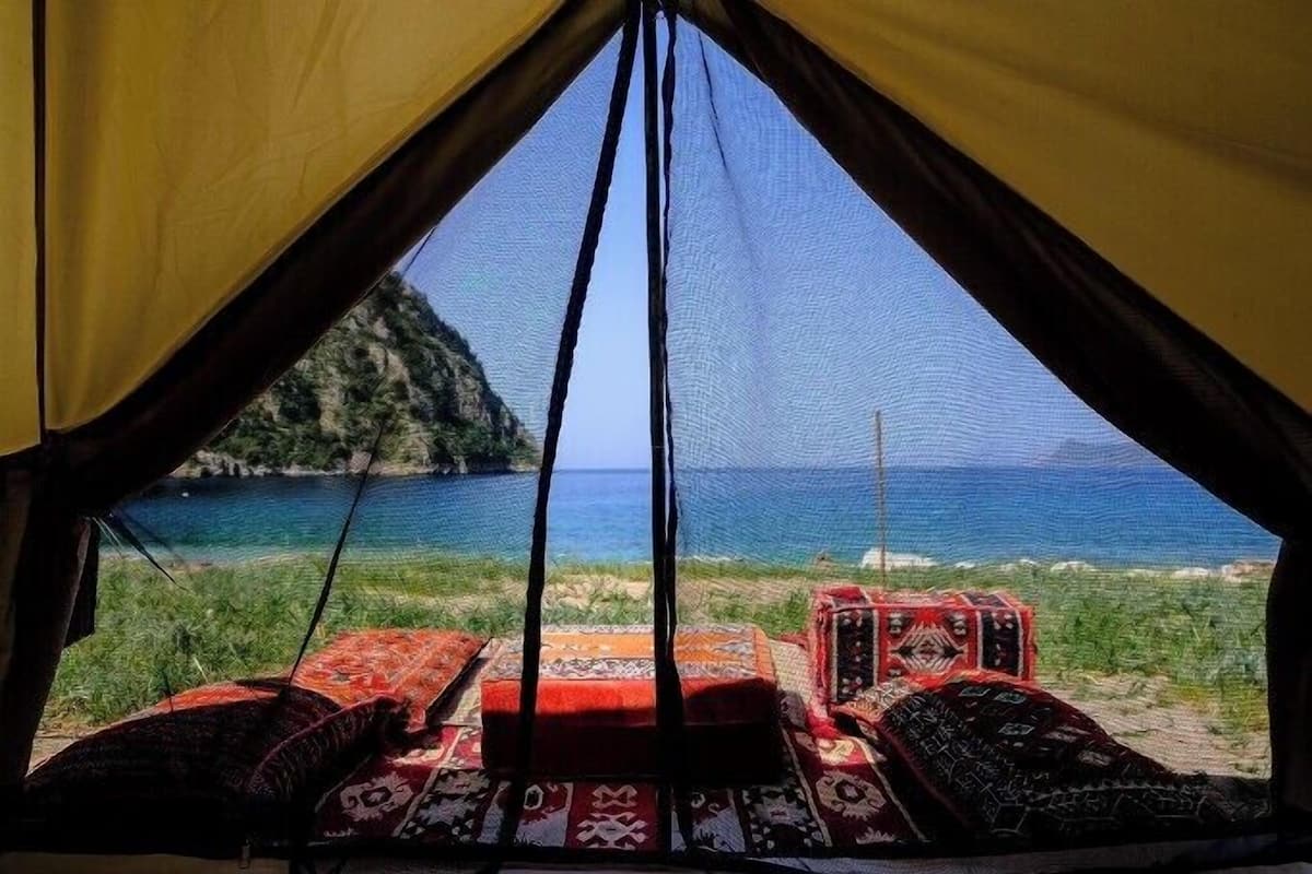 Una carpa con vista al mar y a una montaña. En su interior, alfombras estampadas y una mesita.
