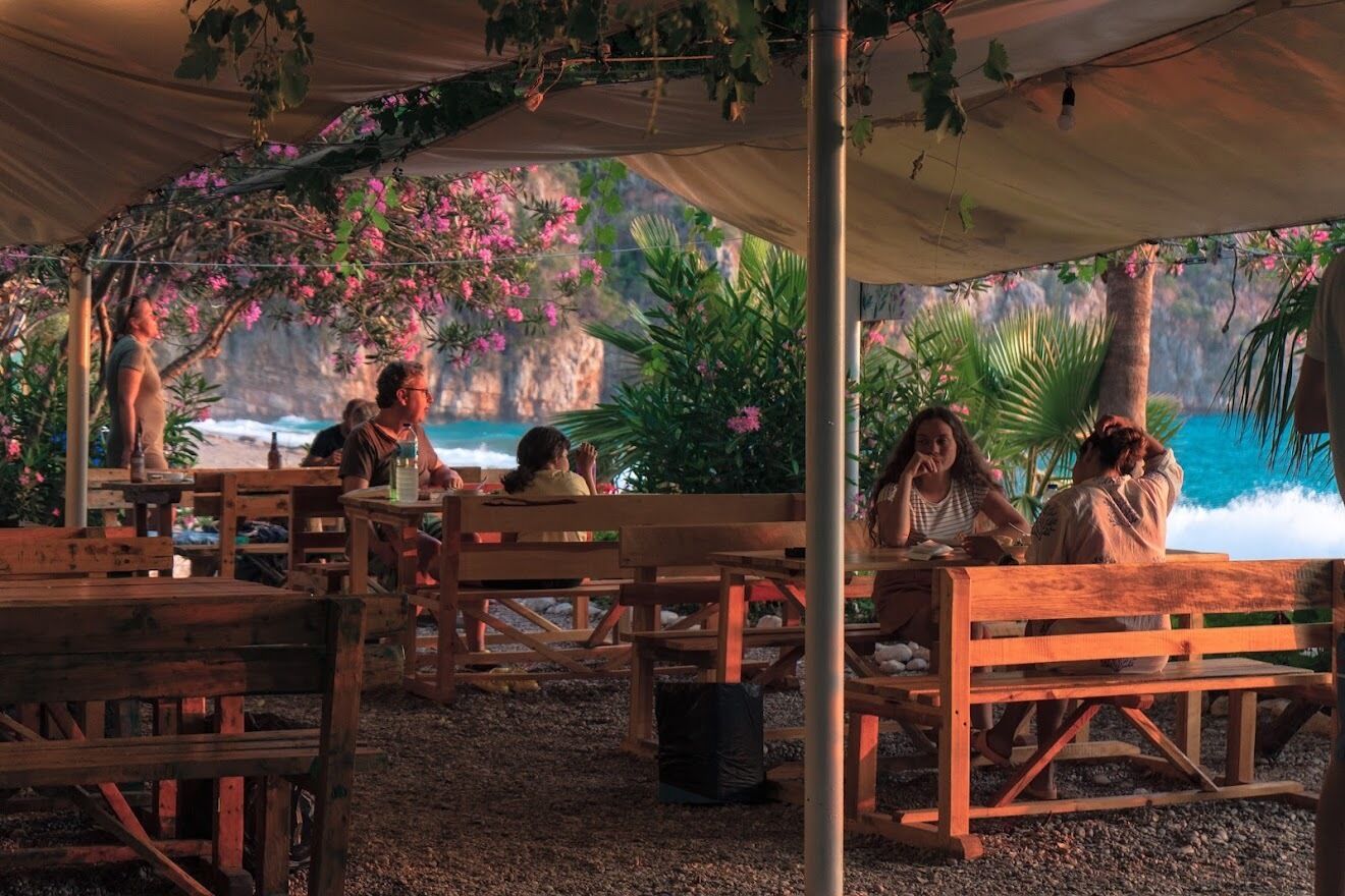 Un espacio al aire libre con bancos y mesas de madera, rodeado de exuberante follaje y flores rosadas.