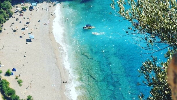 A beach with clear turquoise waters, a boat, and umbrellas. - Kelebekler Vadisi Butterfly Valley (Fethiye)