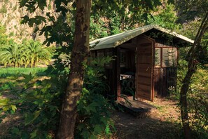 Uma cabana rústica de madeira com telhado inclinado, rodeada por vegetação densa e um cenário montanhoso.