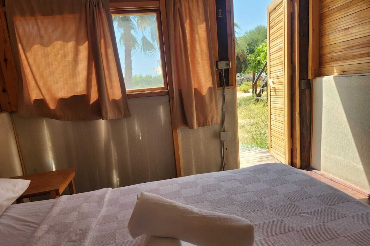 Una habitación con cama, una mesita y una ventana con cortinas.