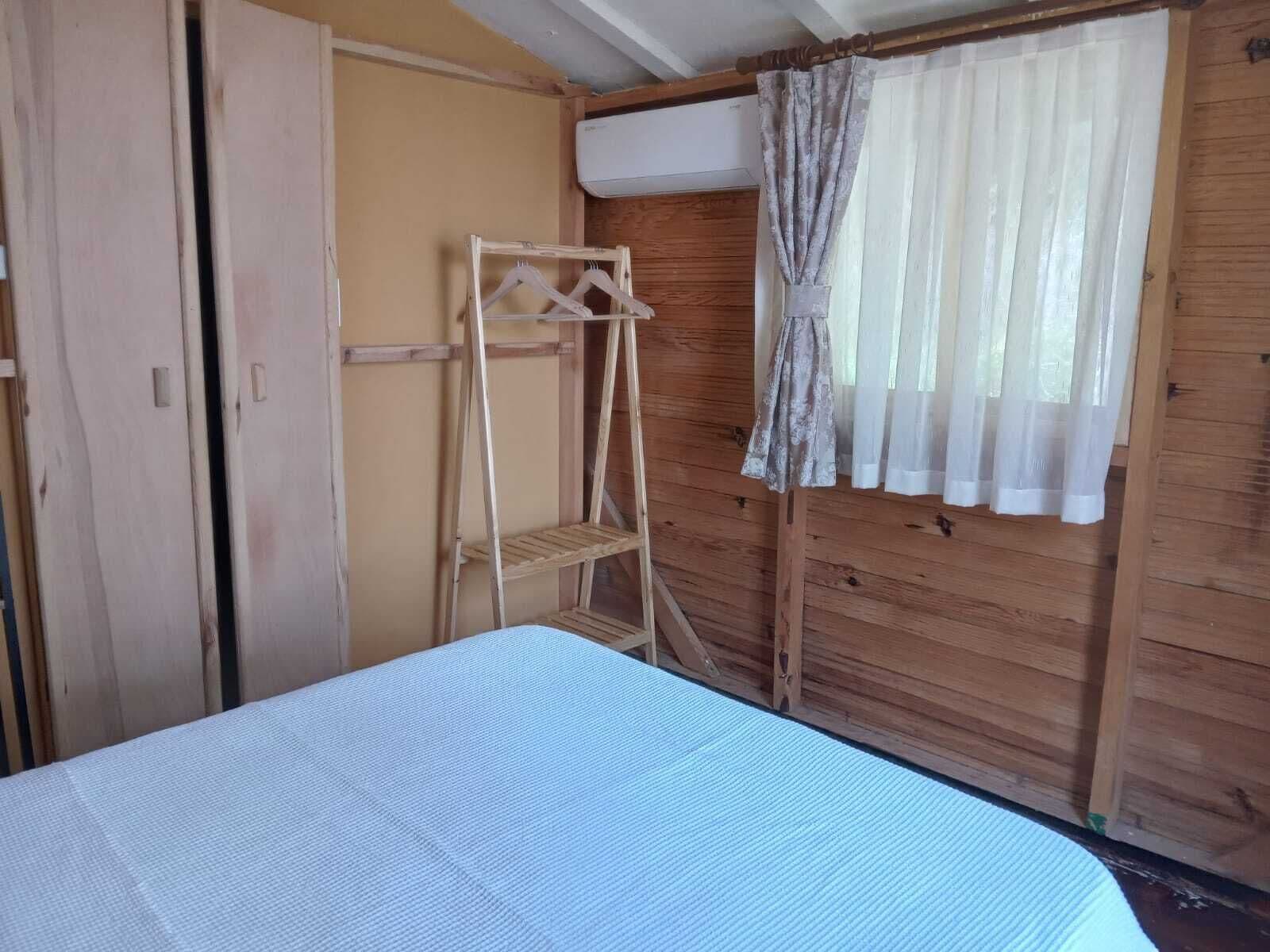 A room with a bed, a wooden wardrobe, a drying rack, and a window with curtains.