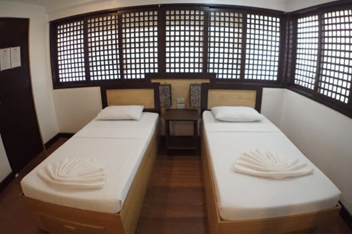 A room with two single beds, wooden headboards, a small table, and a decorative screen.
