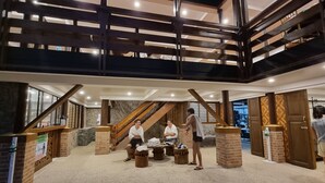 Ein mehrgeschossiges Interieur mit einer zentralen Treppe, Holzbalken und einer Sitzecke mit Tischen und Stühlen.