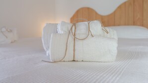 Un letto rifatto con cura, con testiera in legno e copripiumino bianco strutturato.