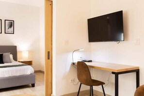 Relax in a serene space with a neatly made bed, flat-screen TV, and comfortable desk area.
