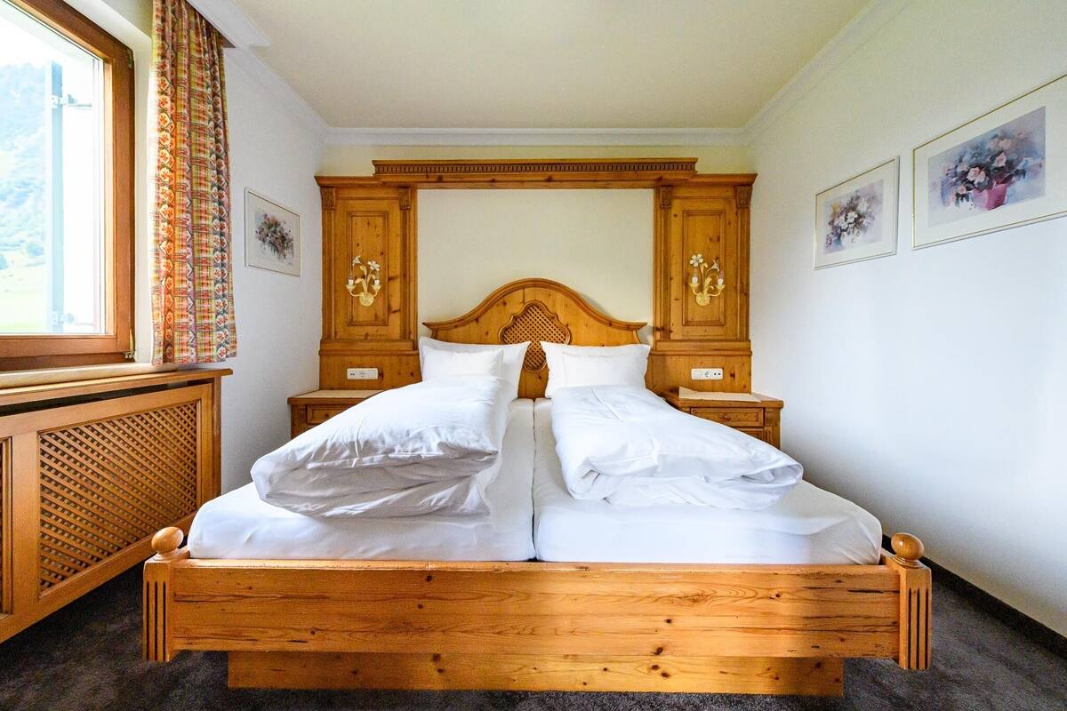 A wooden four-poster bed with white linens, a wooden headboard, and two bedside tables with lamps.