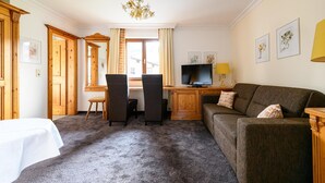 A hotel room with a bed, a sofa, a desk with a TV, and a chandelier. - Montfort (Lech am Arlberg)