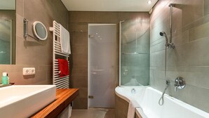 A modern bathroom with a large bathtub, a shower, a wooden vanity, and a towel rack. - Montfort (Lech am Arlberg)