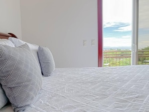 Quarto com cama, almofadas e vista para uma varanda com vegetação.