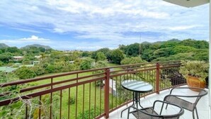 A balcony with a table and chairs, overlooking a lush green landscape with hills and a river.