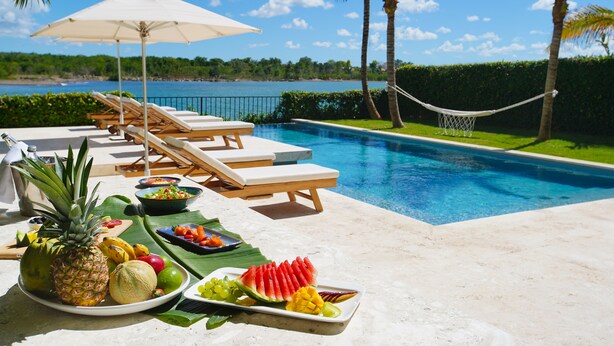 A poolside area with lounge chairs, a hammock, and a fruit platter. - Casa Delfín by Luxe Haus™  – Butlered Villa, Staff, Pool, Golf Carts (La Romana)