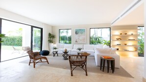 A spacious living room with a white sofa, two wicker chairs, a coffee table, and a bookshelf. - Casa Delfín by Luxe Haus™  – Butlered Villa, Staff, Pool, Golf Carts (La Romana)