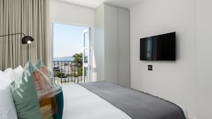 Moderni hotellihuone, jossa on suuri sänky, seinälle asennettu taulutelevisio ja parveke, jolta on näkymä merelle.
