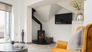A modern living room with a stone fireplace, a round coffee table, a leather armchair, and a TV mounted on the wall. - The Old Piggery -  a cosy fire that sleeps 2 guests  in 1 bedroom (Denbigh)