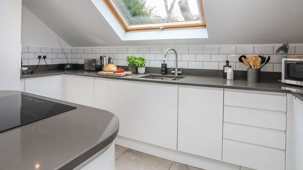 A modern kitchen with a skylight, white cabinets, a black countertop, and a built-in oven. - The Old Piggery -  a cosy fire that sleeps 2 guests  in 1 bedroom (Denbigh)