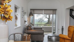 A modern living room with a sofa, a wooden table with candles, and a view of the outdoors. - The Old Piggery -  a cosy fire that sleeps 2 guests  in 1 bedroom (Denbigh)