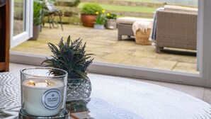 A table with a glass candle labeled "Lime, Basil & Mandarin Aromatic Crisp" and a decorative plant. - The Old Piggery -  a cosy fire that sleeps 2 guests  in 1 bedroom (Denbigh)
