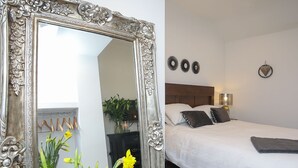 A bedroom with a large ornate mirror, a bed with white linens, a wooden headboard, and decorative wall art. - The Old Piggery -  a cosy fire that sleeps 2 guests  in 1 bedroom (Denbigh)