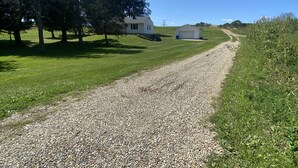 A gravel path leading to a white house with a garage, surrounded by trees and grass. - Countryside- 3 Bedroom Home (Mantua)