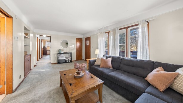 A living room with a dark grey sofa, a wooden coffee table, and a carpeted floor. - Countryside- 3 Bedroom Home (Mantua)