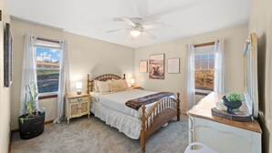 A bedroom with a bed, bedside tables, a nightstand, a dresser, a ceiling fan, and large windows with curtains. - Countryside- 3 Bedroom Home (Mantua)