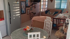 Ein gemütliches Wohnzimmer mit einer Couch, einem Esstisch mit Stühlen, einem an der Wand montierten Fernseher und einem Deckenventilator.