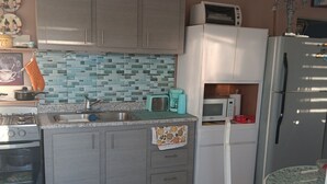 Eine Küche mit grauen Schränken, einer gefliesten Spritzschutzwand, einer Mikrowelle, einem Kühlschrank und einem Esstisch mit Stühlen.