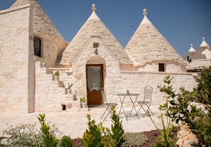 Un edificio de piedra con techos cónicos, una puerta de madera y un patio con sillas de metal.