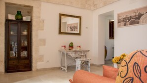 A room with a wooden cabinet, a white table with a mirror, and a sofa with a patterned cushion. - Trullo manivida Mulberry (Locorotondo)