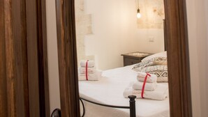 A bedroom with a wooden arched mirror reflecting a bed with white linens and a red towel. - Trullo manivida Mulberry (Locorotondo)