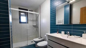 A bathroom with a glass shower enclosure, a white toilet, and a white sink with a mirror above it. - Uncle Pepe House (Valderrobres)