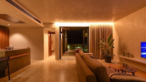 Una sala moderna con un sofá, una mesa de centro y un televisor. Se observa una zona de cocina con una encimera y armarios.