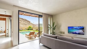 Una sala de estar moderna con un amplio ventanal corredizo que da a una zona de piscina, un sofá cómodo y un televisor de pantalla plana en la pared.