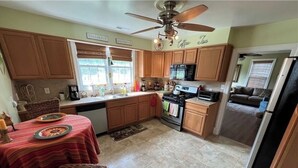 A kitchen with wooden cabinets, a dining table with a red tablecloth, a ceiling fan, and a refrigerator.