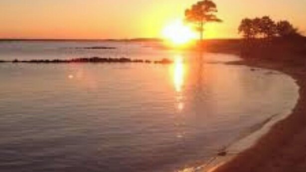 A sunset over a beach with calm waters reflecting the sky.