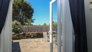 An open sliding glass door leading to a patio with a stone wall, a wooden fence, and a table with chairs. - Ty Glan Morfa (Porthmadog)